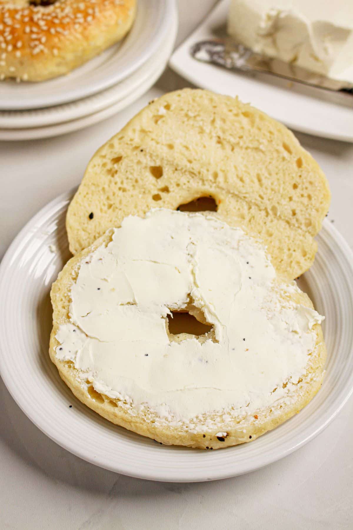 Cream cheese being spread on a cut open flat bagel.