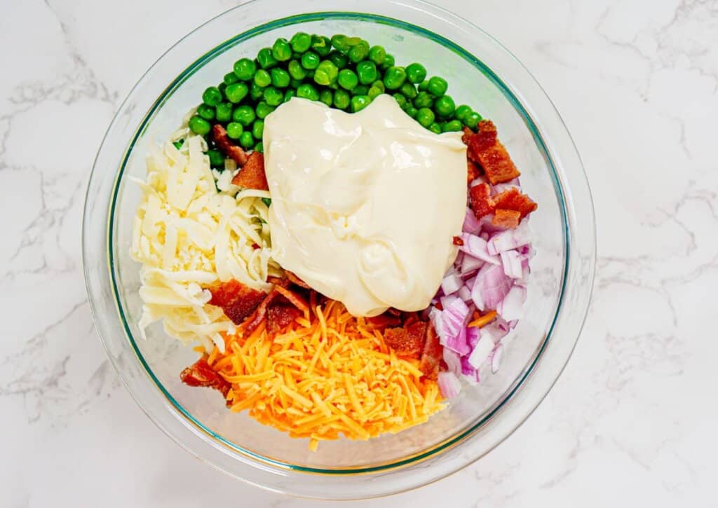 Mayo being added on top of ingredients in a large glass bowl.