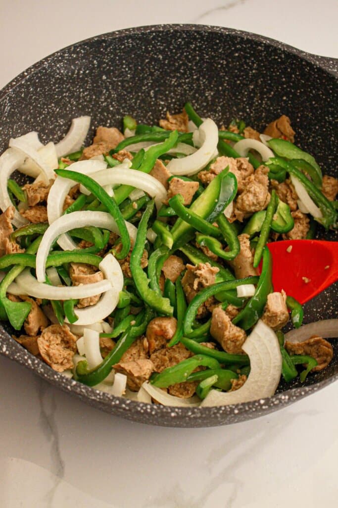 Onions, bell pepper strips and sausage in a skillet.