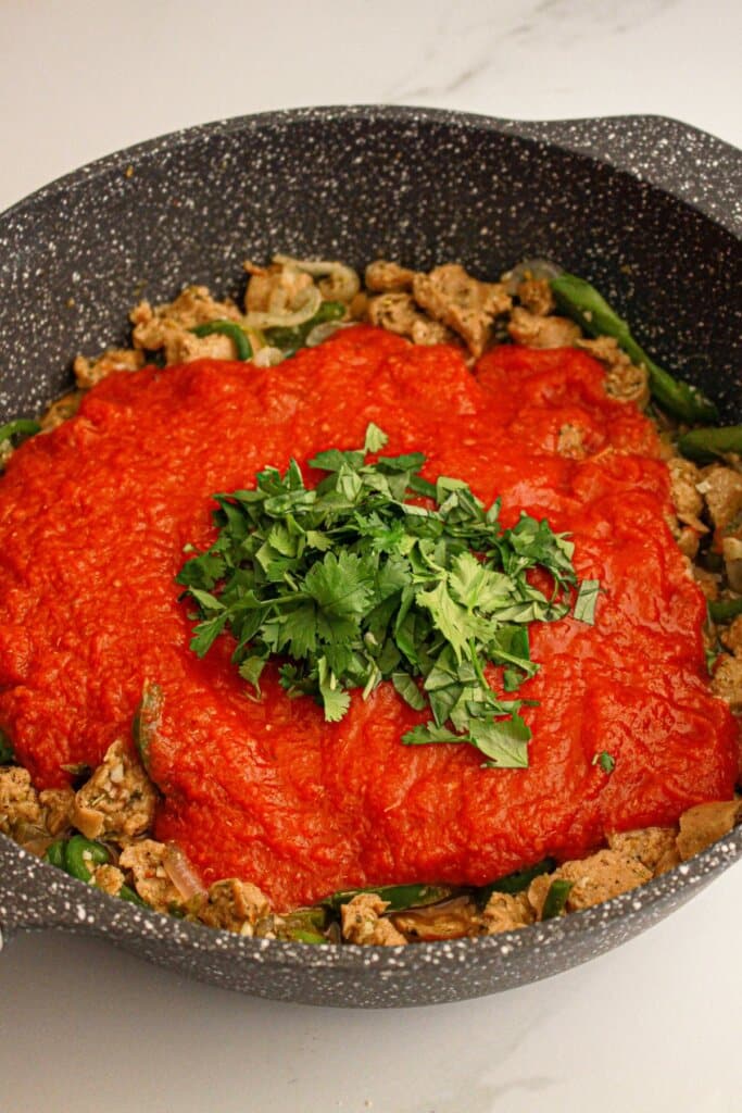 Tomatoes being added to skillet with meat and vegetables.