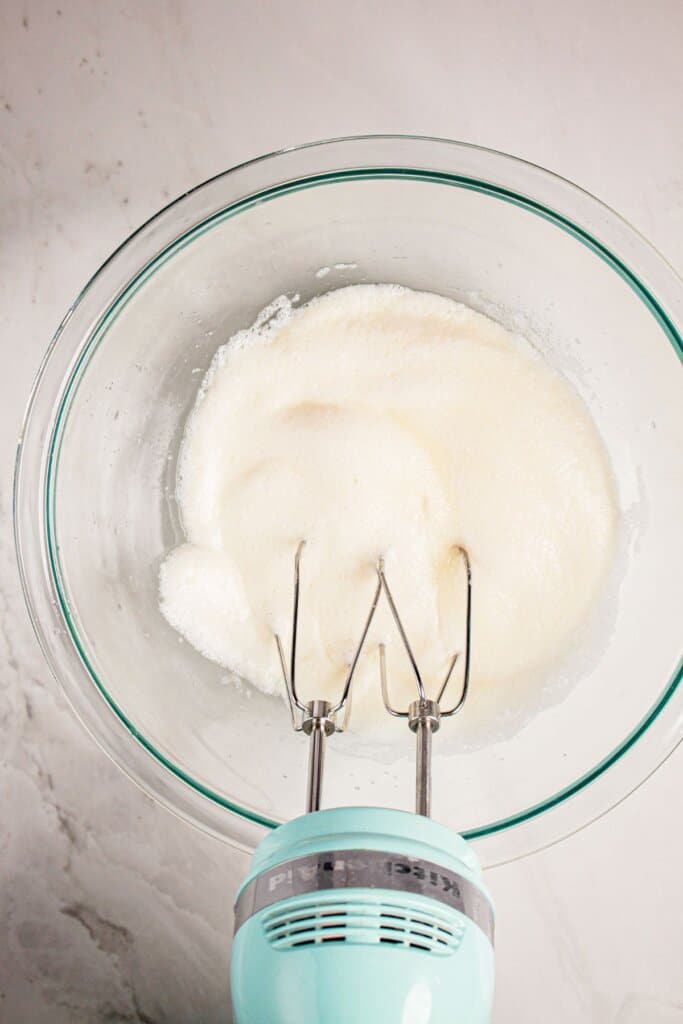 Egg whites being whipped in a mixing bowl with a hand mixer.
