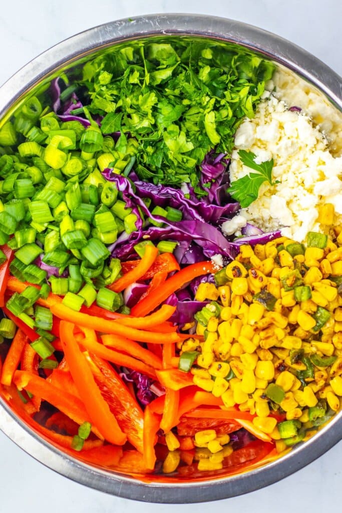Salad ingredients added to a large stainless steel bowl.