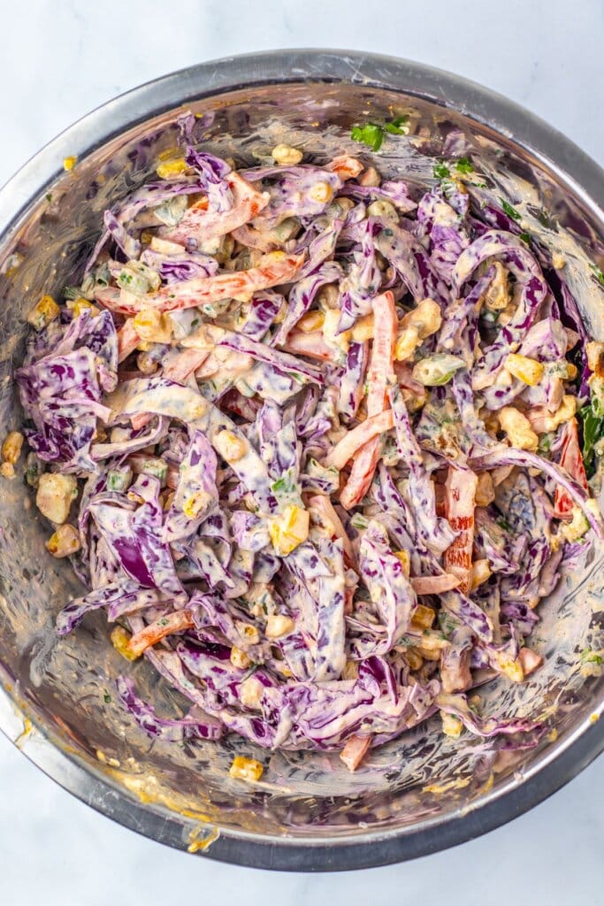 Coleslaw being mixed in a stainless steel mixing bowl.