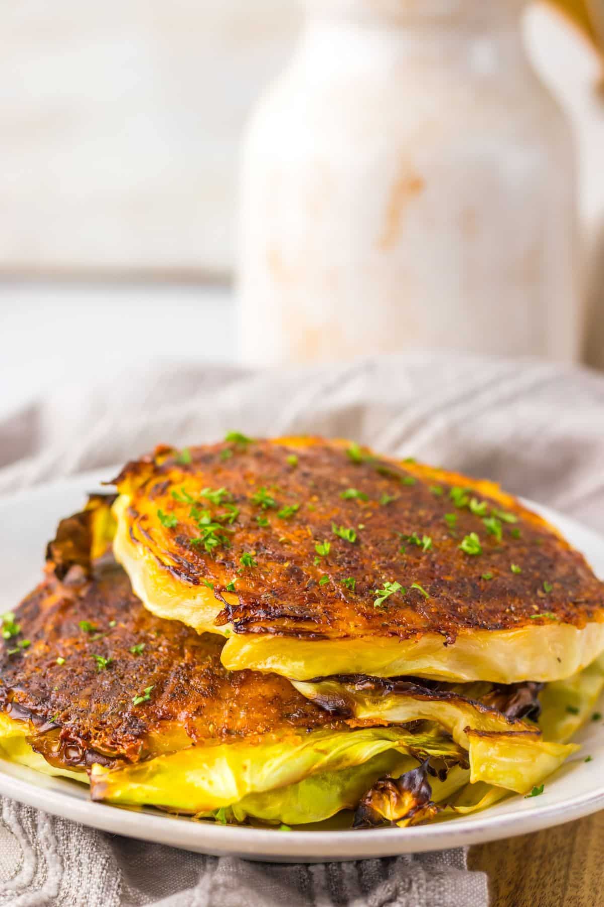 Parmesan cabbage steaks stacked on a white plate.