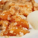 Small plate full of peach cream cheese dump cake with a top of vanilla ice cream.