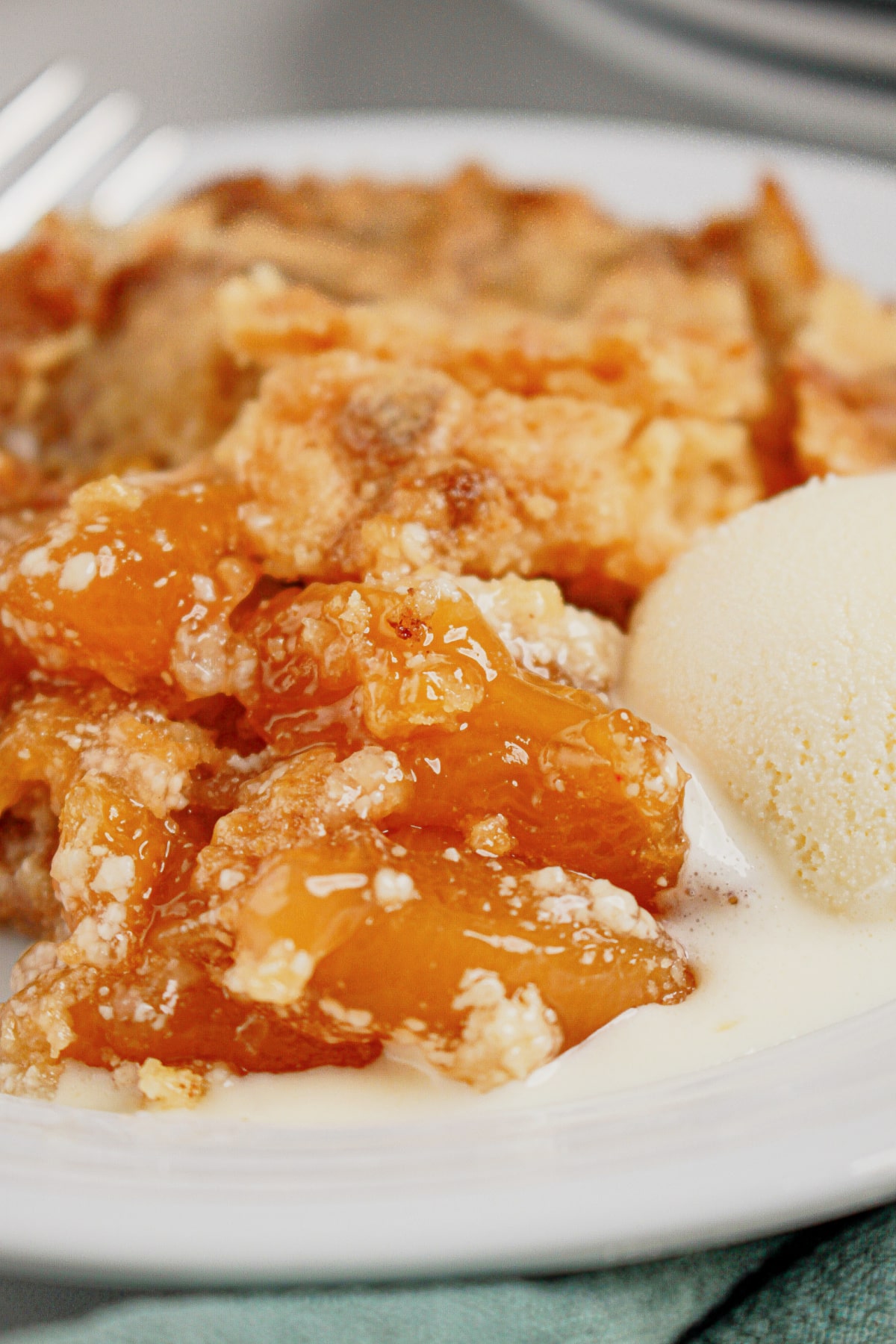 Small plate full of peach cream cheese dump cake with a top of vanilla ice cream.