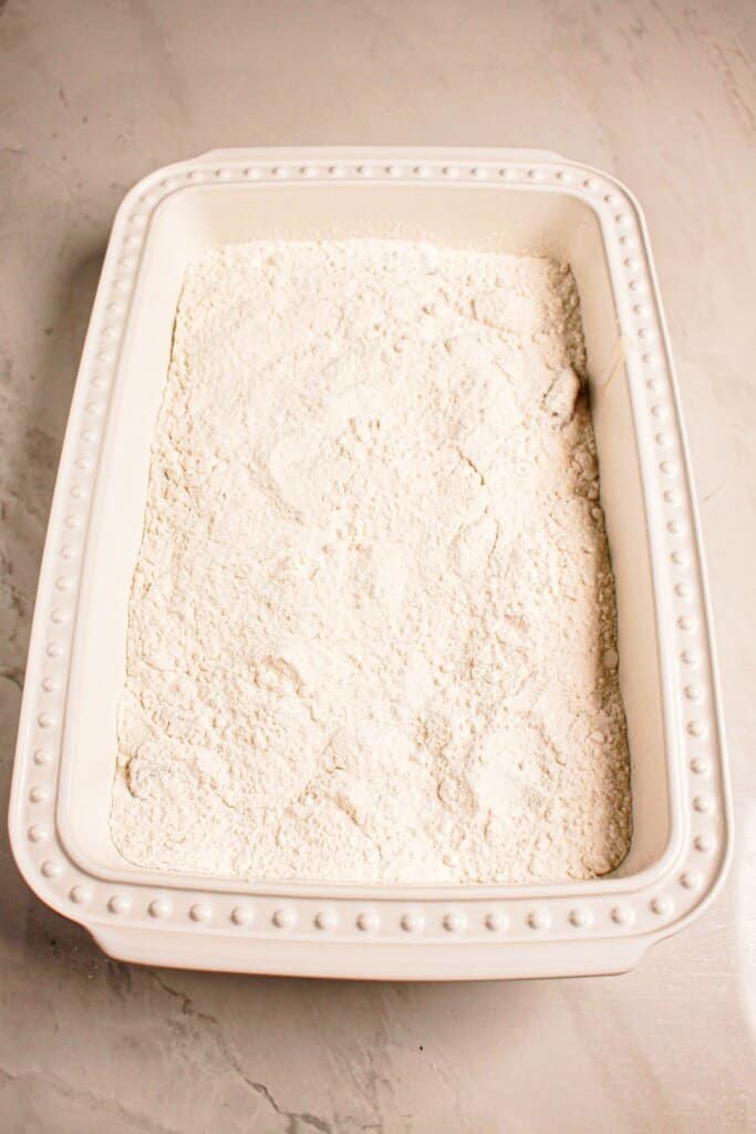 Cake mix being sprinkled on top of this dessert in a baking dish.