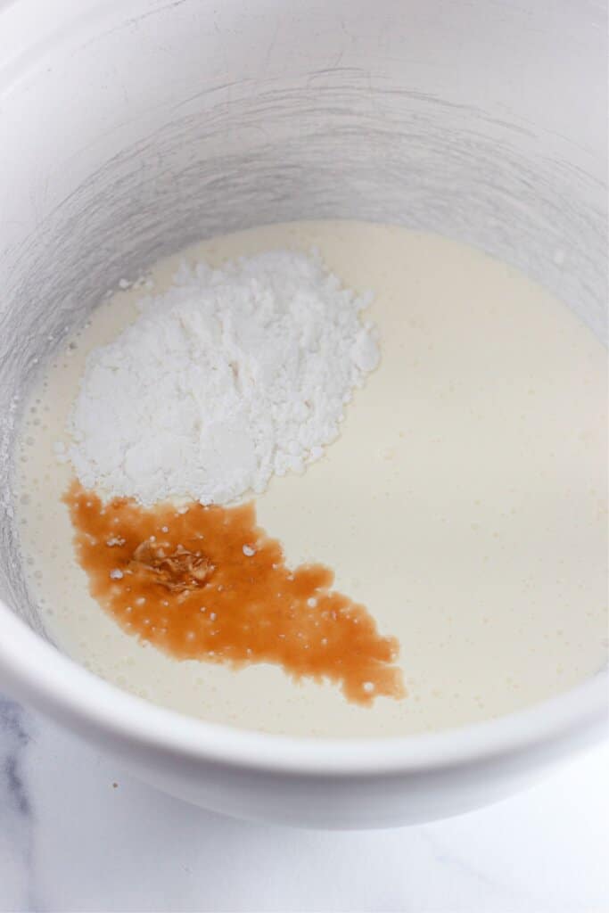 Vanilla and powdered sugar being added to mixing bowl.
