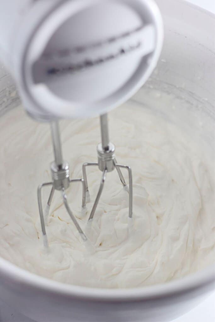 Fluffy topping being mixed in a bowl with a hand mixer.