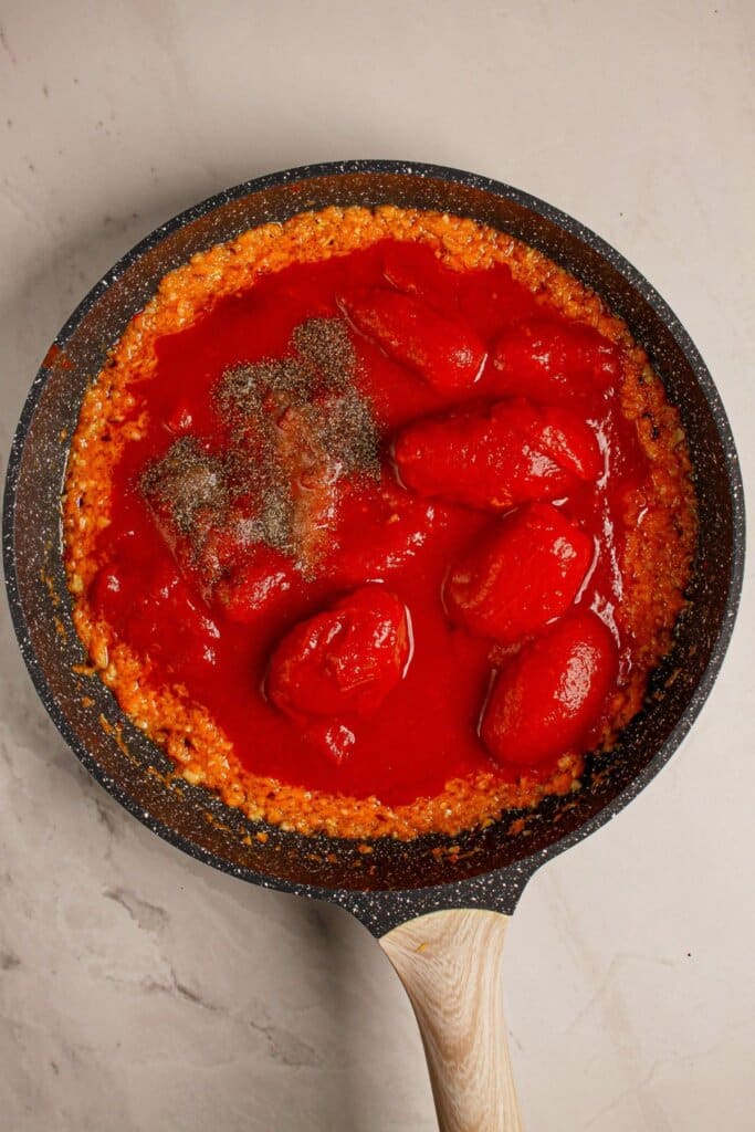 Tomatoes and seasonings added to a skillet.