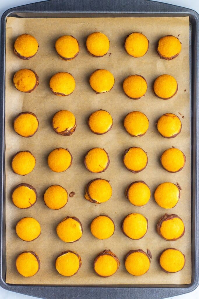 Vanilla wafers on a baking sheet with a Rolo candy sandwiched between them.