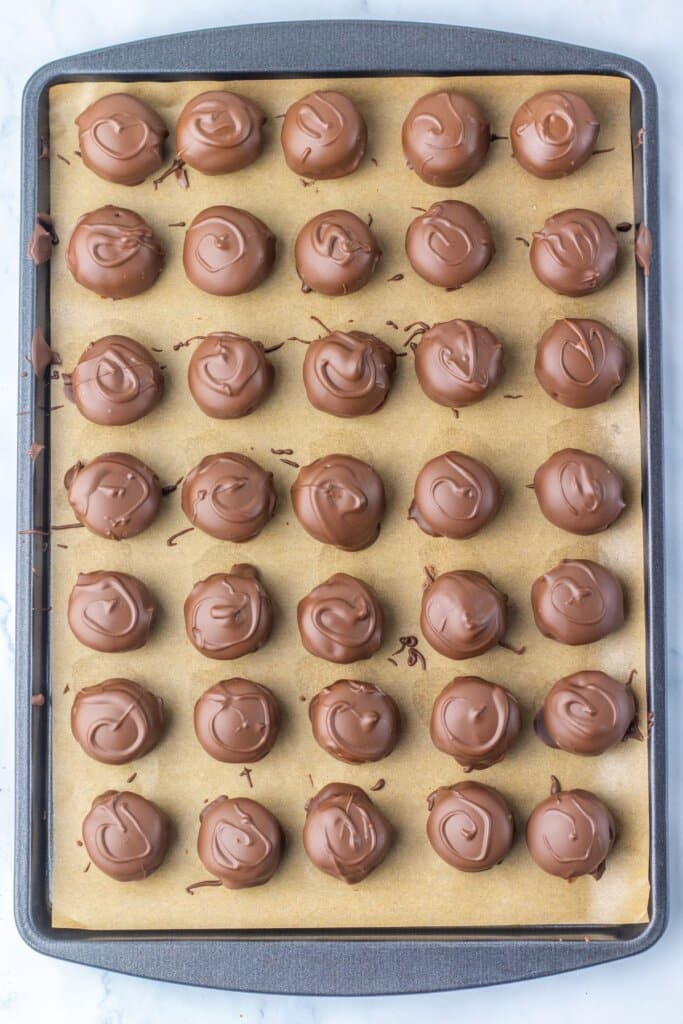 Chocolate being drizzled on top of homemade candy on a baking sheet.