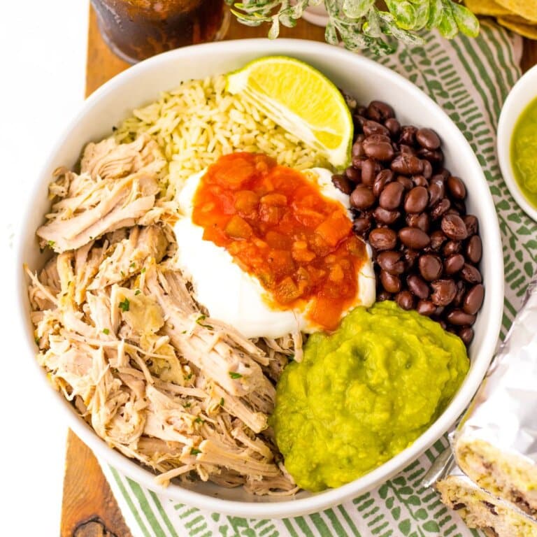 Rice, meat, beans, salsa, guacamole, and sour cream in a white bowl.