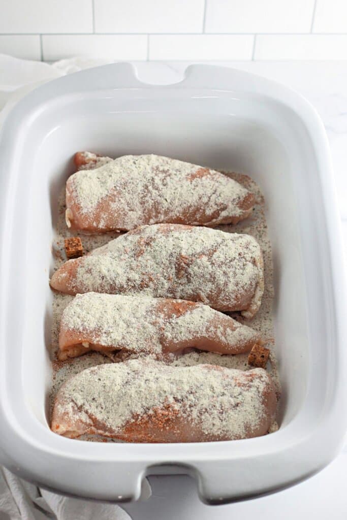 Seasonings being sprinkled on meat in a crock pot.