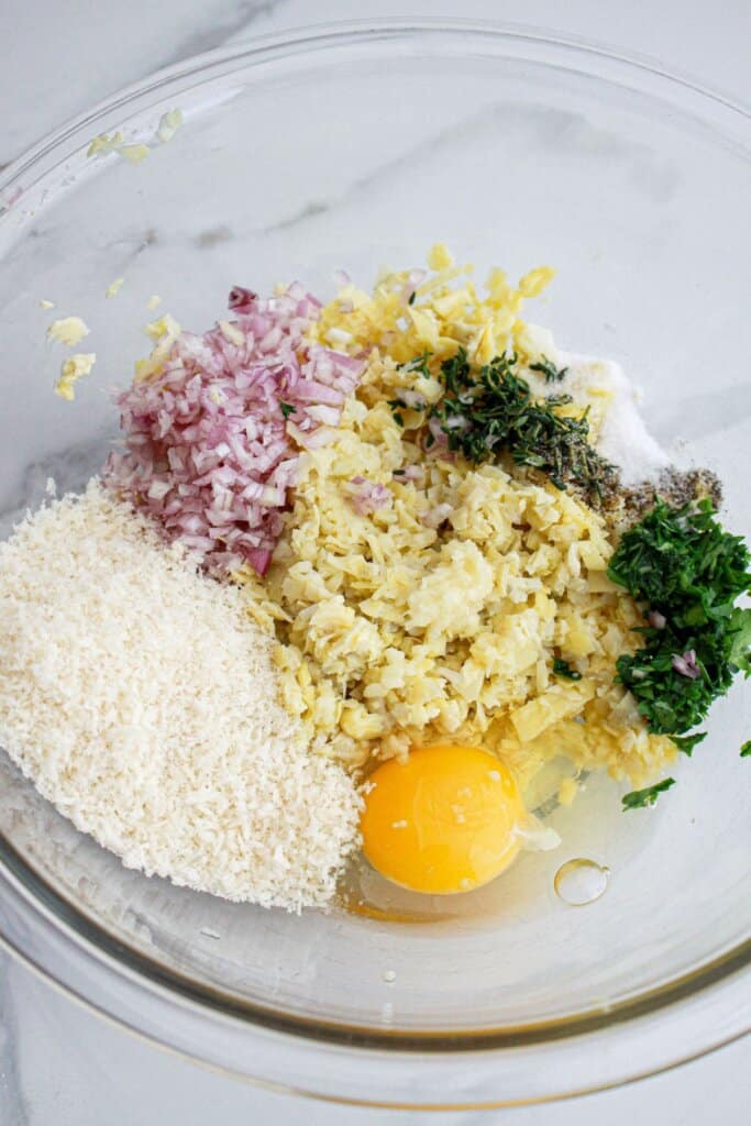 Artichokes, onions, egg, and breadcrumbs in a glass bowl.
