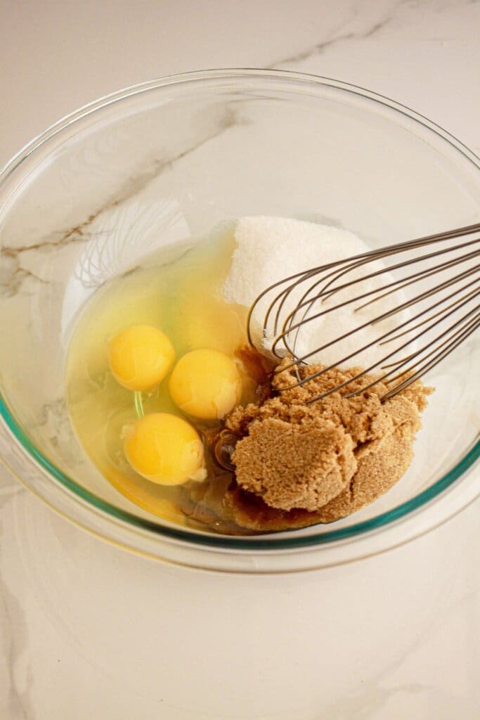 Eggs and sugar being mixed together in a glass bowl.