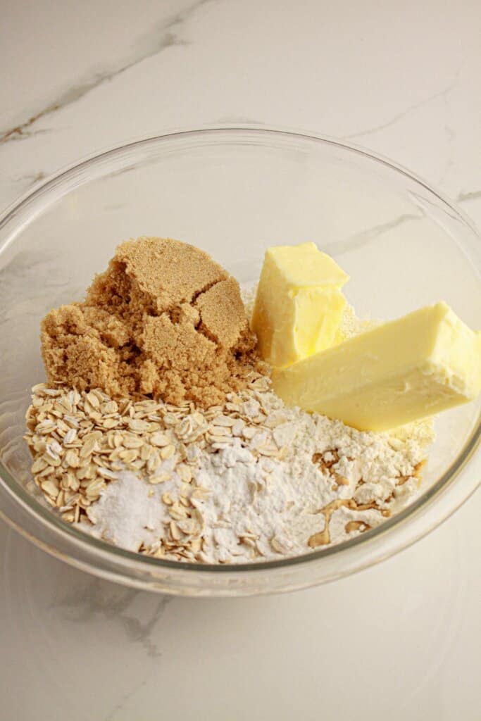 Butter, brown sugar, and oats being mix in a glass bowl.