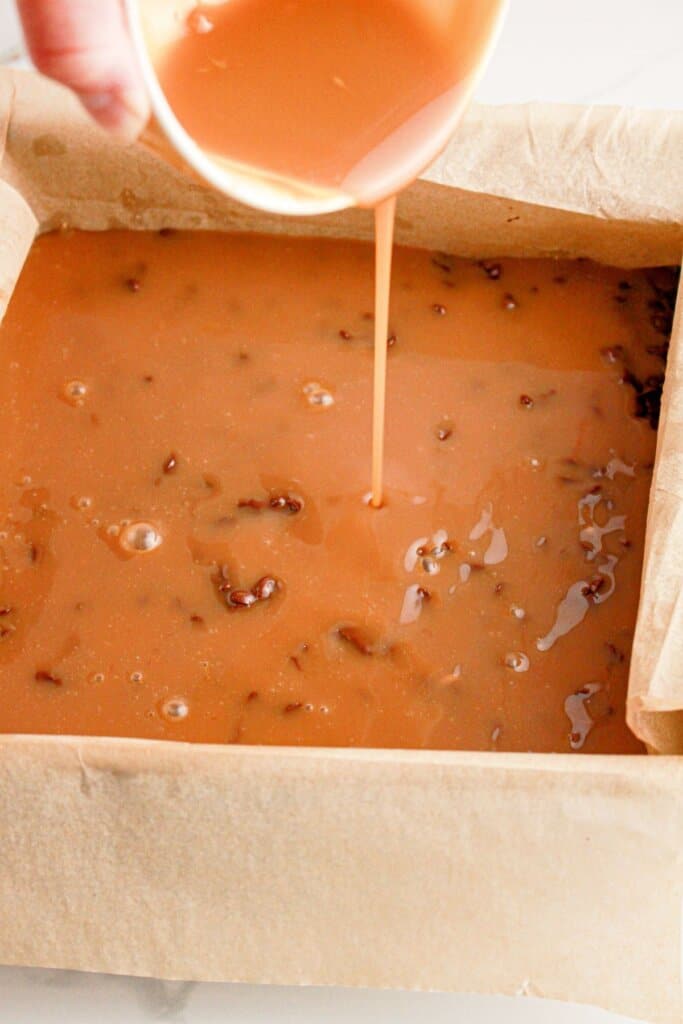Caramel being poured on top of a chocolate in a baking pan.