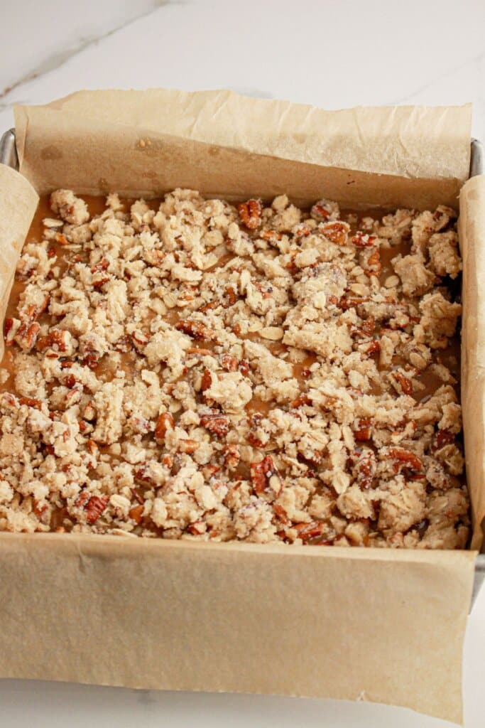 Pecan topping being sprinkled on top of a baking dish.