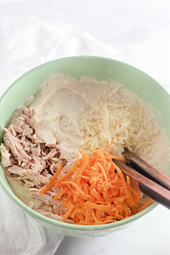 Shredded cheese, meat, and cream of chicken soup being mixed together.