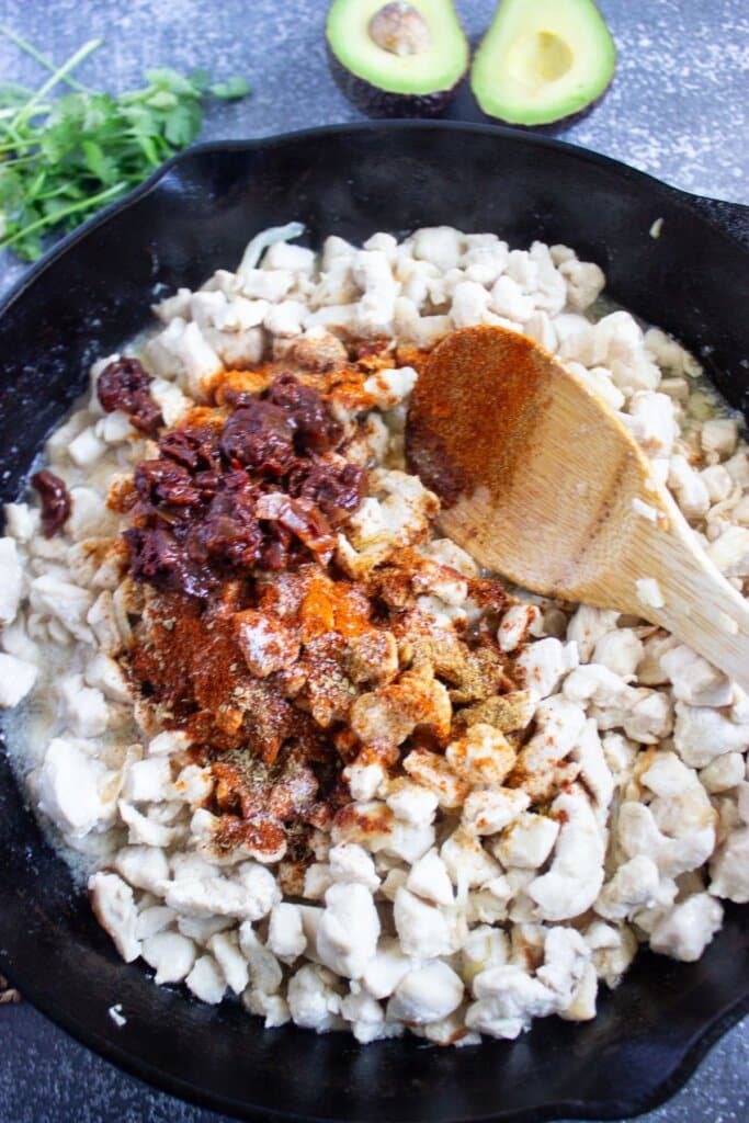 Meat and seasonings being cooked in a cast iron skillet.