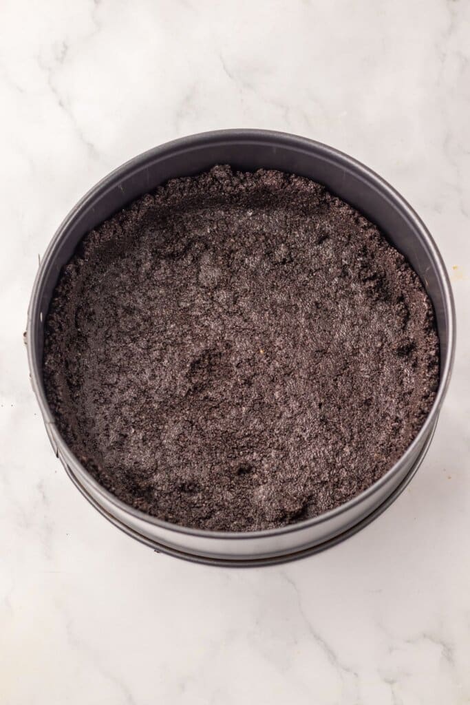 Oreo crust being pressed into a springform pan.