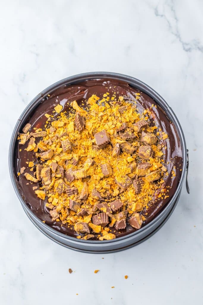Candy bars being added to the top of a cheesecake.