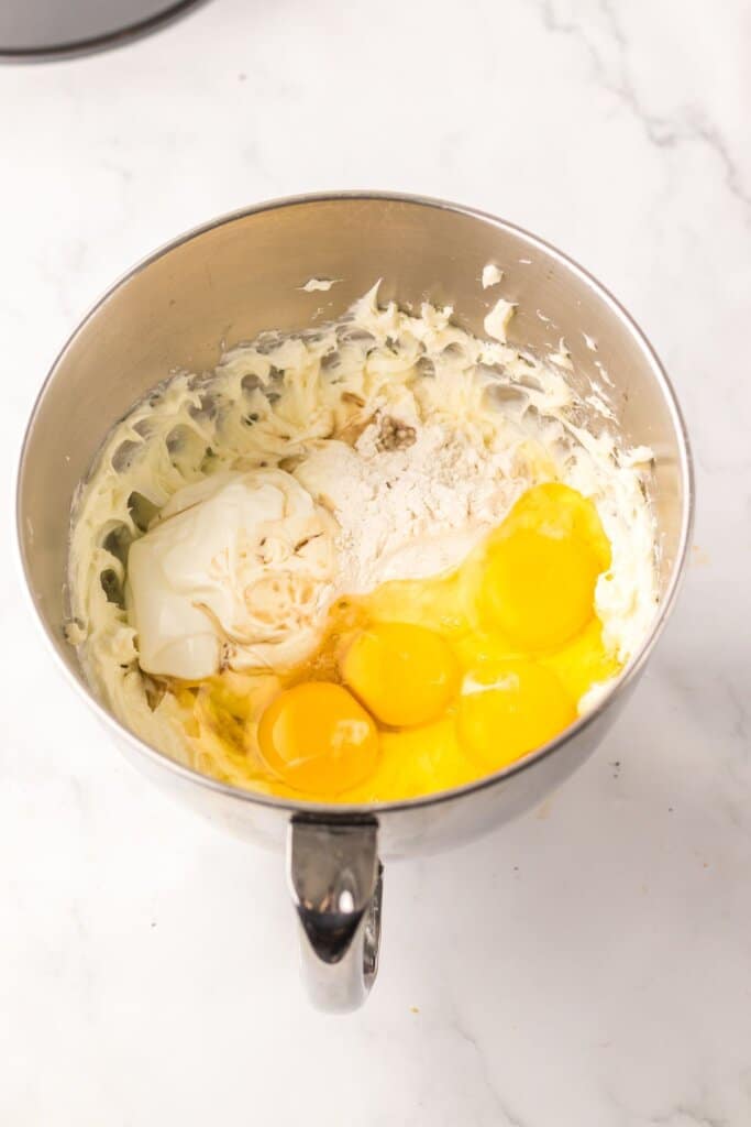 Eggs being added to cream cheese in a mixing bowl.