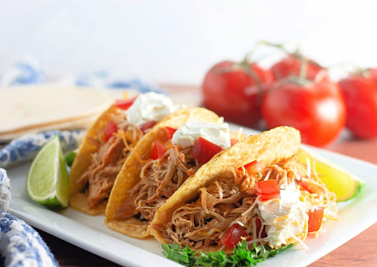 Three Mexican shredded chicken tacos on a plate.
