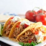 Three Mexican shredded chicken tacos on a plate.
