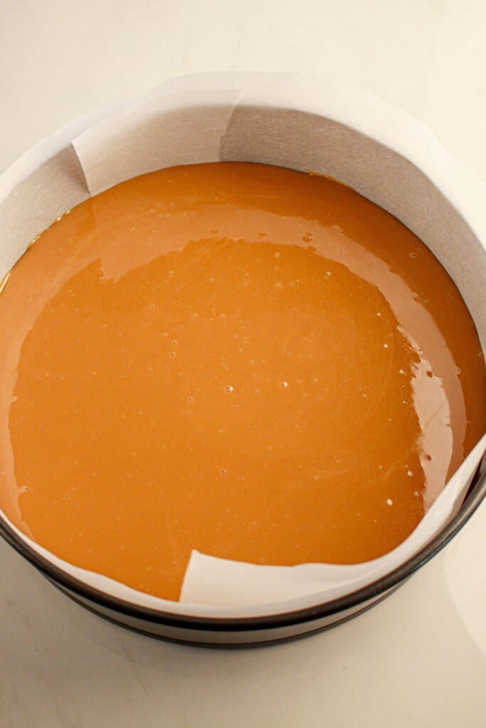 Caramel poured into a parchment lined springform pan.