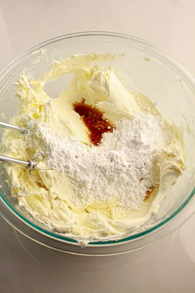 Powdered sugar and vanilla being added to cream cheese.