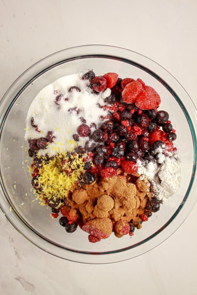 Fruit, sugar, and lemon zest being mixed in a glass bowl.