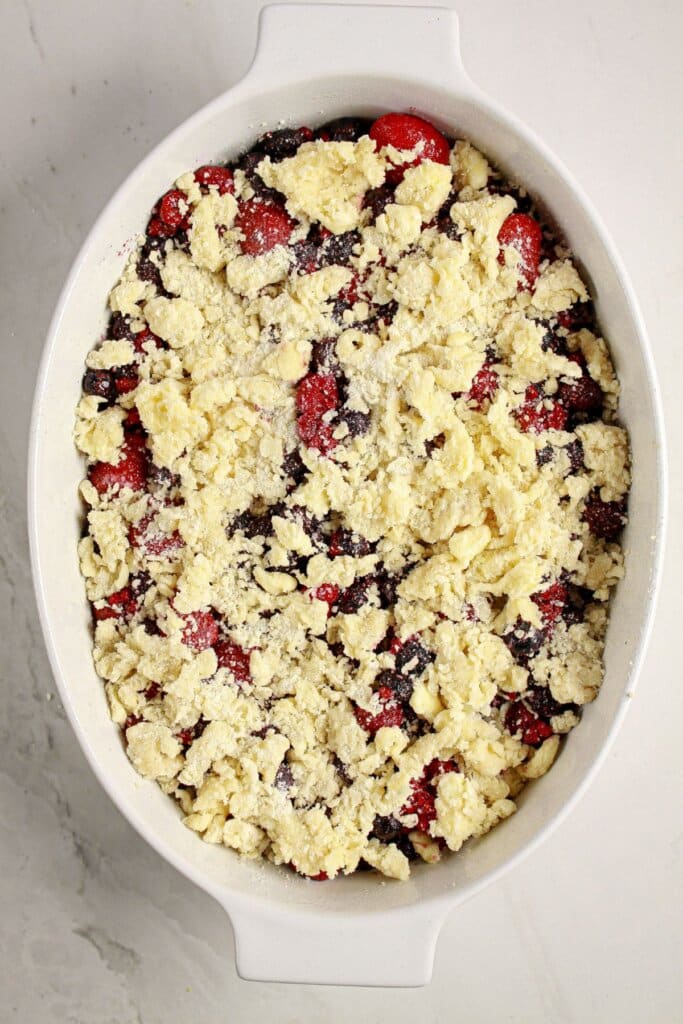 Topping being sprinkled on top of fruit in a baking dish.