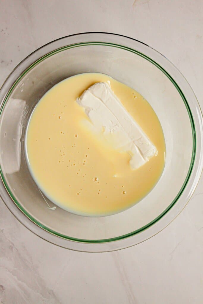 Cream cheese and condensed milk being mix in a glass bowl.