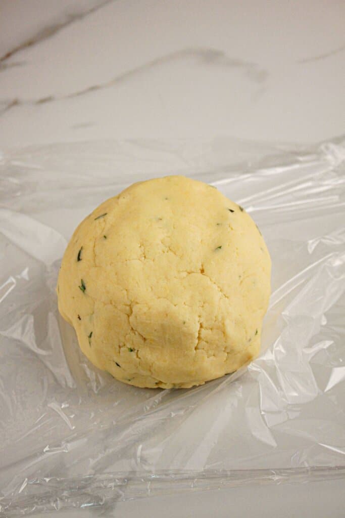 Dough ball being wrapped in plastic wrap.