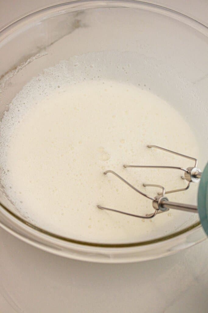 Meringue being mixed in a glass bowl.