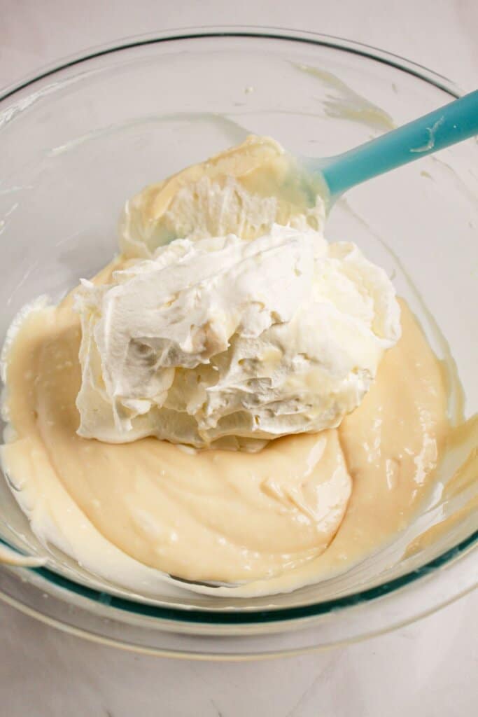 Whipped cream being added to cream cheese in bowl.