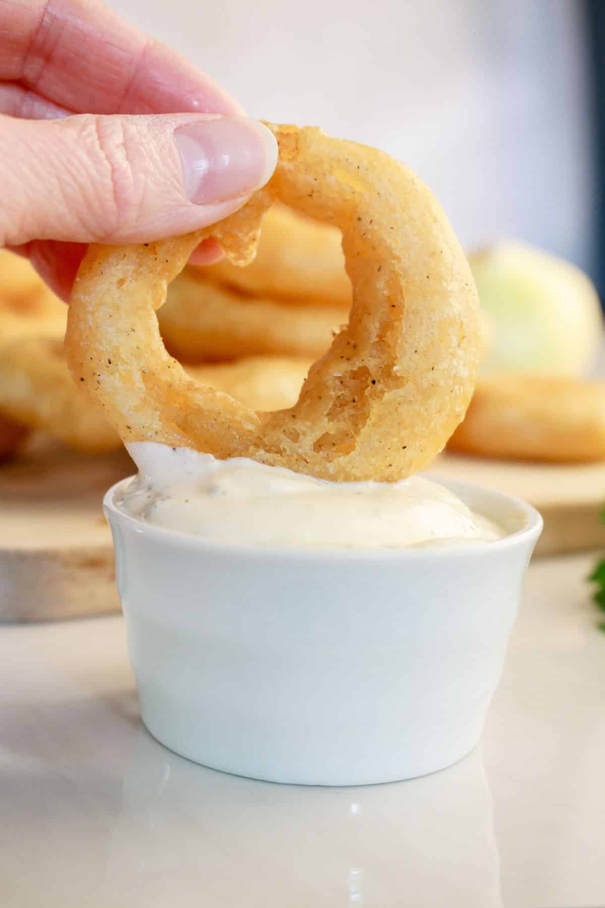 Onion ring being dipped in sauce.