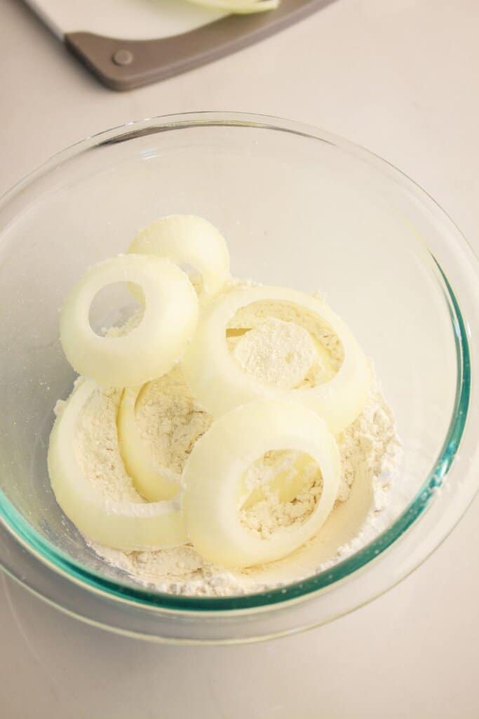 Onions being coated in flour in a glass bowl.