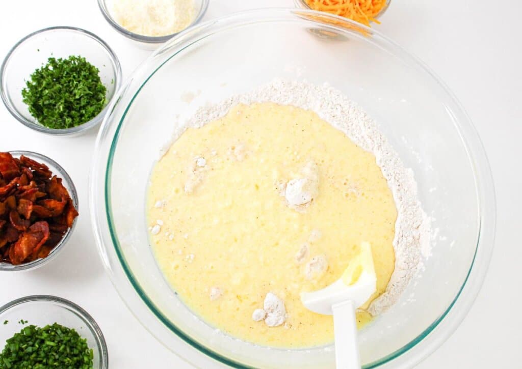 Wet ingredients being added to dry ingredients in a glass bowl.