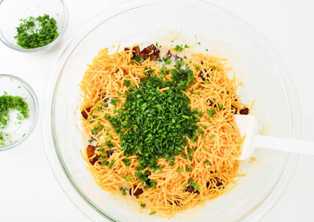 Cheese being added to batter in a glass bowl.