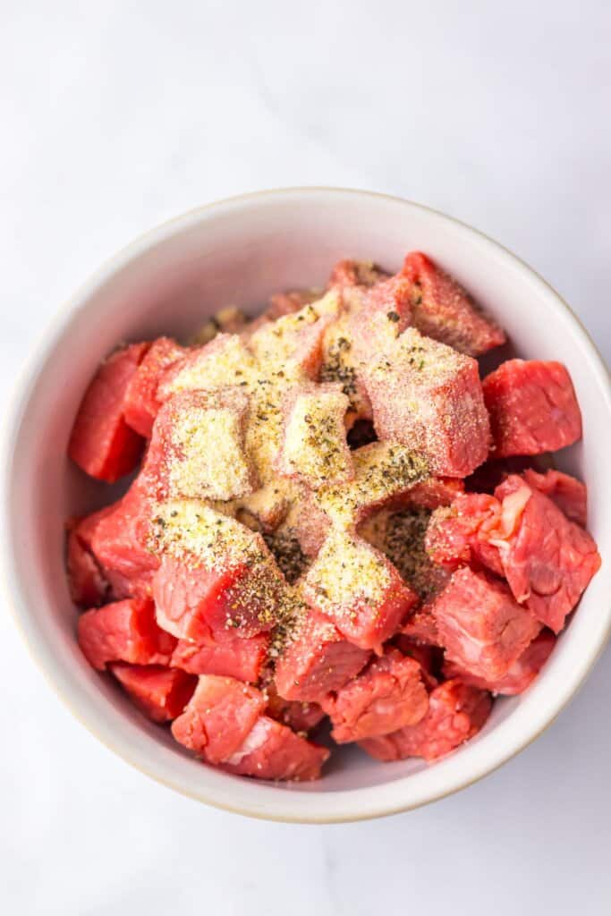 Beef cubes being seasoned in a small bowl.