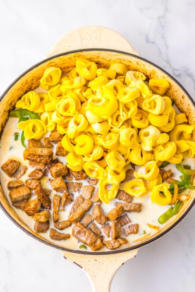 Pasta being added to a pan with meat and sauce.