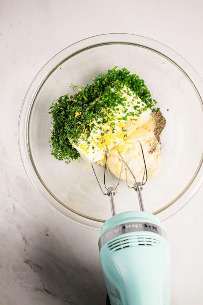Cream cheese and seasonings being mixed in a glass mixing bowl.