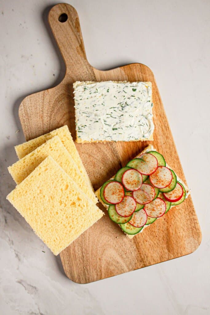 Radishes being added to the top of bread on a cutting board.