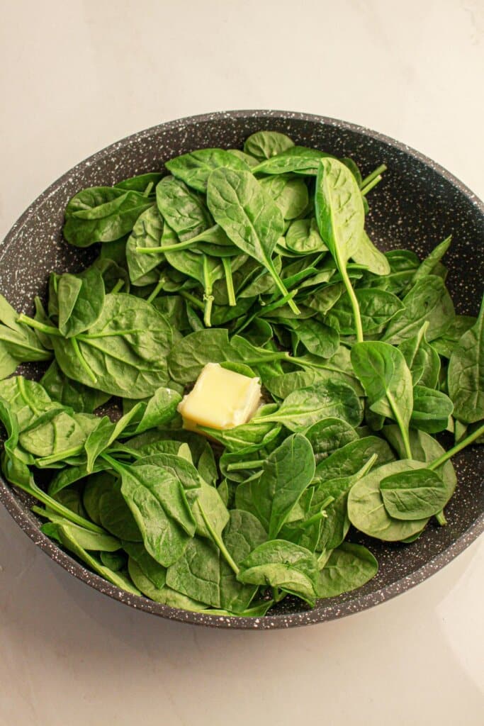 Spinach wilting with butter in a skillet.