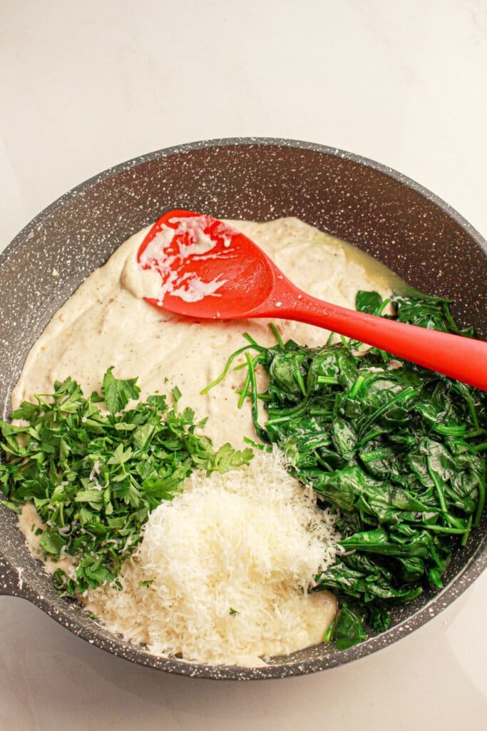 Herbs and cheese being stirred into a sauce.