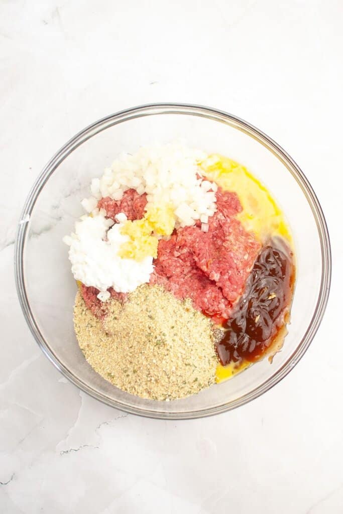 Ground beef and ingredients being mixed in a glass bowl.