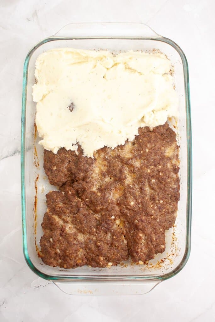 Potatoes being spread on top of meatloaf.